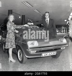 1975, historisch, in einem Autosalon, übergab ein Verkäufer in einem Nadelstreifenanzug die Schlüssel für einen neuen Wagen, einen Vauxhall Chevette, an eine glückliche Kundin, England, Großbritannien. Der Stylist Chevette, ein kleines Familienauto, wurde von Vauxhall Motors in Großbritannien zwischen 1975 und 1984 hergestellt. Mit einem Design, das auf dem Opel Kadett basierte, war der Chevette einer der ersten in Großbritannien gebauten Heckklappen und von 1975 bis 1978 das meistverkaufte Modell Großbritanniens in dieser Klasse. Stockfoto