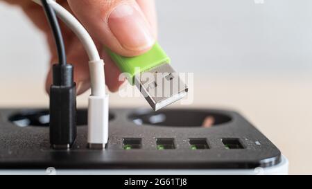 Modernes praktisches Multi-Port usb-Ladegerät für Geräte. Nahaufnahme einer Handsteckdose, die mehrfarbige Kabel in eine Steckdose einsteckt. Makro. Stockfoto