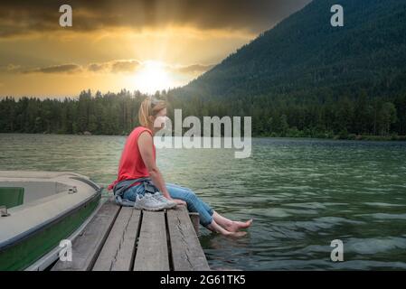 Junge Frau, die sich am Pier am See entspannt Stockfoto