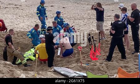 Newquay, Großbritannien. Juli 2021. Newquay, Cornwall, Fistral Beach. 18:00 Stunden. Ein männlicher Urlauber wurde von Sand verschlungen, als ein tiefes Loch aus losem Sand in den Strand einstürzte und ihn vergrub. Strandgänger und Rettungsschwimmer gruben verzweifelt, bis die Rettungsteams von Küstenwache und Feuerwehr eintrafen. Es wird angenommen, dass der Unfall durch Quetschungen verletzt wurde und dass freigelegter Sauerstoff aus Kanistern bereitgestellt wurde. Ein Mitglied der Küstenwache wird gesehen, wie er einen Tropfen auf den Unfallopfer anwendet. Alle vier Notfalldienste nahmen an dem Vorfall Teil. Juli 2021. Kredit: Robert Taylor/Alamy Live Nachrichten Stockfoto