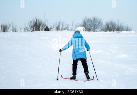 Eine Frau in einer blauen Jacke, die einen verschneiten Hang hinauffährt. Stockfoto