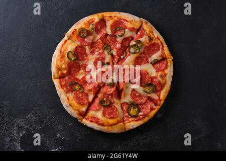 Pepperoni Pizza mit Jalapeno-Paprika. Eine Nahaufnahme einer Pizza. Flach liegend. Auf einem dunklen Hintergrund. Stockfoto