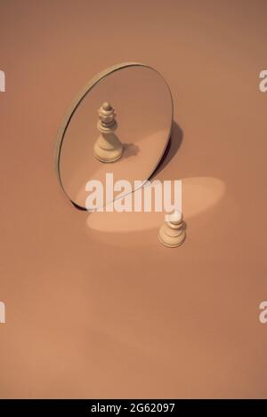 Schachfiguren aus Holz, Spielfigur und Königin, die sich in einem Spiegel spiegeln. Auf modischem Pastellhintergrund. Optische Täuschung. Pfand ist potenzielle Königin Konzept. Stockfoto