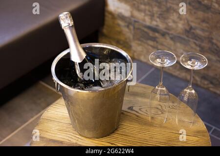 Champagner-Flasche im Kühler, Eimer mit Eis und zwei Sektgläser auf Holztisch. Romantisches Dinner und Party-Konzept Stockfoto