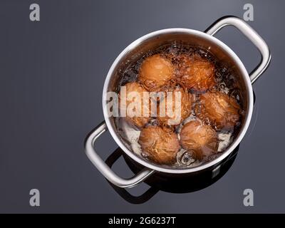 Hühnereier kochen in einem Topf auf einem Glaskeramikkochfeld. Kochen hart gekochte Eier in einer Metallpfanne auf einem Elektroherd. Eier in einem Topf anbraten. Stockfoto