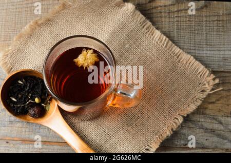 Ein Glas mit duftendem, gebrühtem Blumentee auf einem Holztisch mit einem Holzlöffel. Draufsicht. Selektiver Fokus. Stockfoto