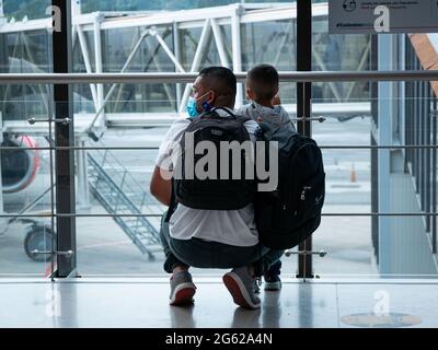 Medellin, Antioquia, Kolumbien - Mai 17 2021: Lateinischer Vater mit seinem Sohn mit Maske Blick nach draußen auf den Flughafen Jose Maria Cordova Stockfoto