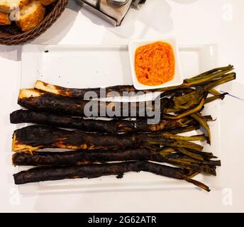 Calcots Zwiebeln werden auf dem Teller mit Romesco-Sauce serviert - ein traditionelles katalanisches Gericht Stockfoto