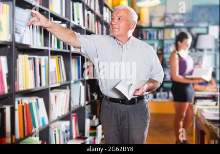 Der 61-67-jährige Mann wählt das Buch Stockfoto