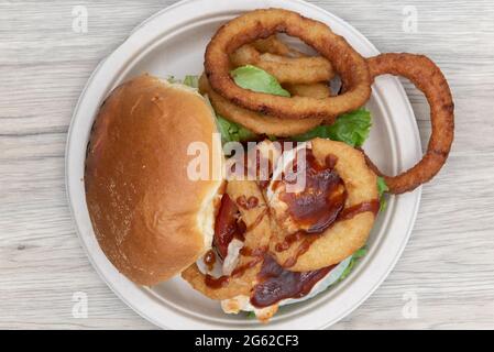 Blick von oben auf das hoch im getoasteten Brötchen gestapelte Hühnchen-Sandwich mit riesigen Zwiebelringen an der Seite, um den gesamten Teller zu füllen. Stockfoto