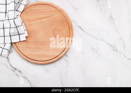 Leere Pizzaplatte aus Holz mit Serviette und Nudelholz auf einem Küchentisch aus Marmorstein. Stockfoto