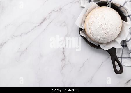 Frischer roher, hausgemachter Hefeteig, der in einer gusseisernen Pfanne auf einem Marmortisch liegt. Stockfoto