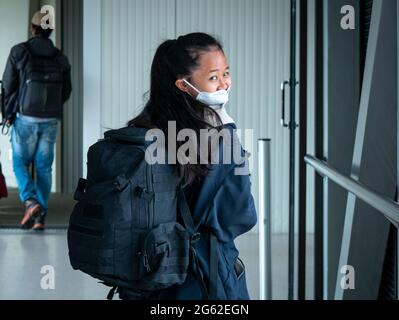 Medellin, Antioquia, Kolumbien - 17 2021. Mai: Kleine Asiatin mit Maske geht mit Rucksack über den Gang zum Flugzeug Stockfoto