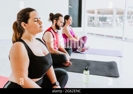 Plus Größe junge hispanische Frau sitzt während der Meditation während Yoga-Sitzung in Lateinamerika Stockfoto