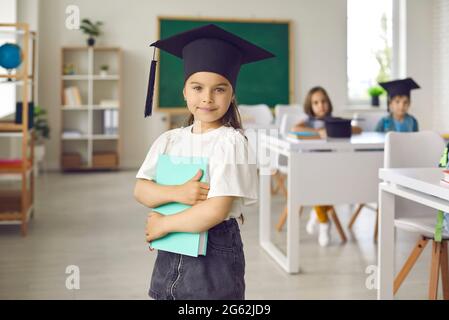 Porträt eines niedlichen kleinen Grundschulabsolventen Mädchen, das einen akademischen Grad Hut trägt. Stockfoto