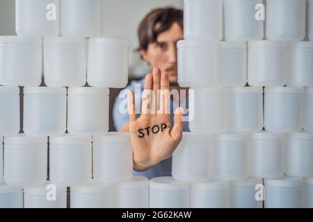 Mann, der Halt zeigt, umgeben von vielen Gläsern Joghurt, die er in einem Jahr verwendet. Eine riesige Menge von Plastikbehältern für Lebensmittel. Übermäßiger Verbrauch von Kunststoff Stockfoto
