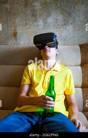 Junger Mann in VR-Brille hält eine Flasche Bier auf dem Sofa Stockfoto