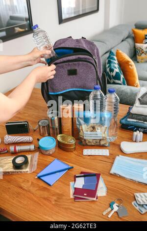 Frau, die eine Wasserflasche zur Vorbereitung eines Notfallrucksacks legt Stockfoto