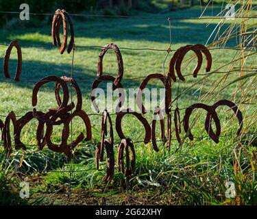 Alte rostige Hufeisen, die kopfüber an einem Drahtzaun hängen, Neuseeland. Stockfoto