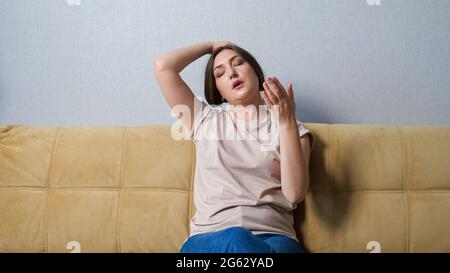 Junge Frau, die unter Hitze leidet, während sie zu Hause auf dem Sofa sitzt. Stockfoto