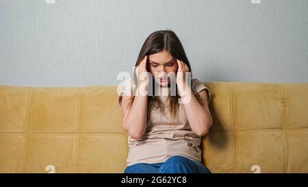 Junge Frau, die Kopfschmerzen hat, während sie auf dem Sofa sitzt. Stockfoto