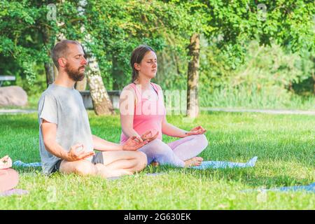 Paar machen draußen oder draußen Yoga auf dem Gras im Park bei Sonnenuntergang Stockfoto