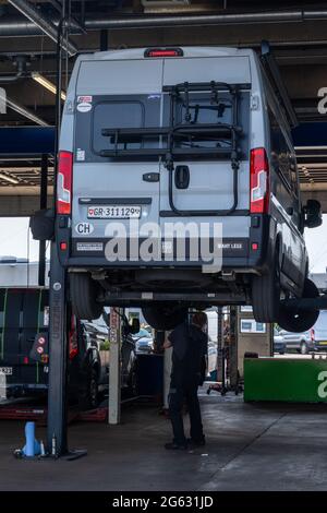 Odense, Dänemark - 10. Juni 2021: Grauer Wohnmobil in einer modernen Garage auf dem Autolift mit einem Mechaniker darunter Stockfoto