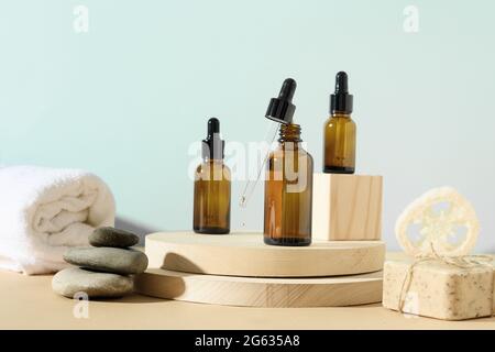 Minimale moderne natürliche Zusammensetzung mit Kosmetiköl in Flaschen, Naturstein, Loofa auf Ständer auf beige und blauem Hintergrund. SPA-Set für die Körperpflege. Stockfoto