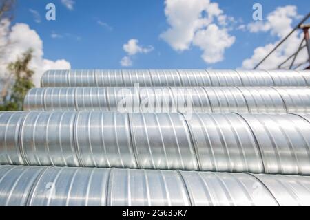 Lüftungsrohre gegen den blauen Himmel. Stahlrohre, Teile für den Bau von Luftkanälen für eine industrielle Klimaanlage in einem Lager Stockfoto