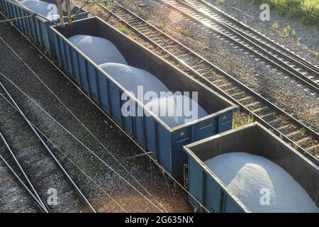 Beladene Eisenbahnwaggons fahren auf Schienen. Güterzug mit weißem Kies, Draufsicht Stockfoto