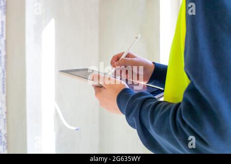 Bauingenieur hält einen Tablet-Computer. Nahaufnahme mit dem Mobiltelefon auf der Baustelle. Architekt in gelber Sicherheitsjacke Zeichnung auf Laptop. Forem Stockfoto