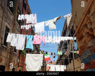 In der engen Straße der typisch italienischen Stadt hängen viele Kleidungsstücke, die in der Sonne trocknen Stockfoto