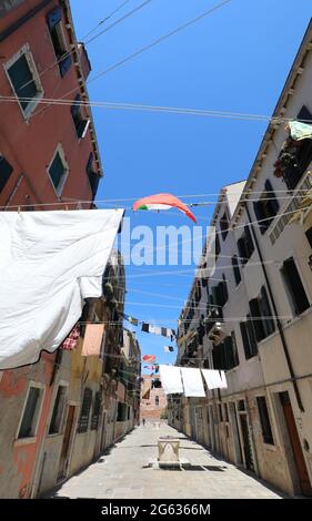 In der für die Insel Venedig in Italien typischen engen Straße hängen viele Kleidungsstücke, die in der Sonne trocknen Stockfoto