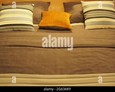 Bettfragment mit gestreiften und monochromen quadratischen Kissen und einer Decke in graubraunen Farbtönen