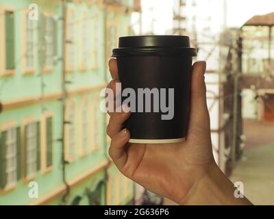 Eine Frauenhand hält schwarzes Glas aus Pappe mit Kaffee. Nahaufnahmen Stockfoto