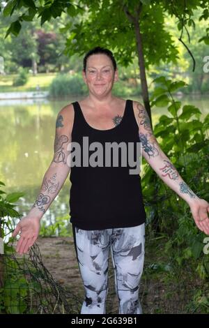 Posierte Porträt einer attraktiven Frau mittleren Alters zeigt ihre mehrere Arm Tattoos. In einem Park in Queens, New York.p Stockfoto