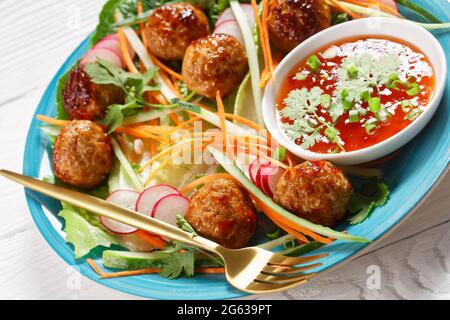 Vietnamesischer Banh-mi-Salat mit Fleischbällchen, Karotten, Gurken und Rettich, serviert über Salat mit Rosenkohm auf einem blauen Teller mit süßer Chilisauce Stockfoto