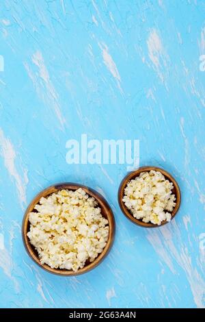 Schüsseln Popcorn in kleinen und großen Portionen auf blauem Hintergrund. Das Konzept von Freizeit und Unterhaltung. Vertikales Foto Stockfoto