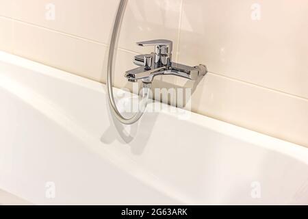 Neuer moderner Metallwasserhahn mit der weißen Badewanne auf dem Wandhintergrund mit Keramikfliesen im Badezimmer. Stockfoto