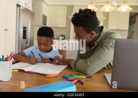 Glücklicher afroamerikanischer Vater mit Sohn, der zu Hause Hausaufgaben macht und lächelt Stockfoto