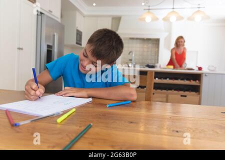 Kaukasische Mutter in der Küche und ihr Sohn machen Hausaufgaben lächelnd zu Hause Stockfoto