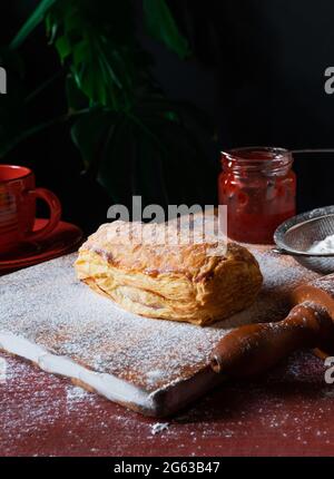 Fresh Puff mit Pflaume oder rote Johannisbeere Marmelade auf dem Tisch mit einer roten Tasse und Glas Marmelade auf dem schwarzen Hintergrund besetzt. Stockfoto