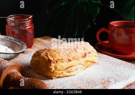 Fresh Puff mit Pflaume oder rote Johannisbeere Marmelade auf dem Tisch mit einer roten Tasse und Glas Marmelade auf dem schwarzen Hintergrund besetzt. Stockfoto