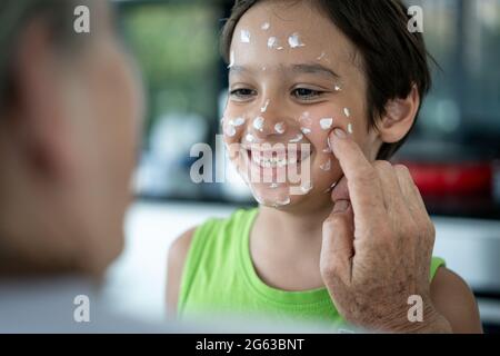 Großmutter und kleiner Junge, die Creme-Schutz auf ihr Gesicht legen Stockfoto