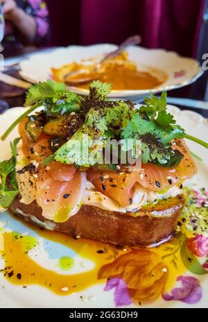 Offenes Sandwich oder französische Tartare mit geräuchertem Lachs, Avocado, Zucchini-Brötchen, Basilikum und gehacktem Schnittlauch auf einer gerösteten Scheibe Sauerteig Stockfoto