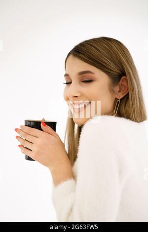 Junge lächelnde schöne glückliche Frau mit langen Haaren genießen Cappuccino auf weißem Hintergrund. Beauty Frau genießt Kaffee. Tasse heiße Getränke. Stockfoto