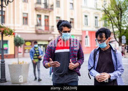 Zwei junge multirassische Freunde in Masken, die im Freien chatten Stockfoto