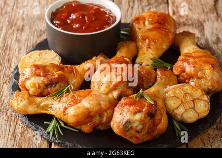 Würzige Grillhähnchen Beine mit Knoblauch und Rosmarin serviert mit bbq-Sauce close-up auf einem Schieferbrett auf dem Tisch. Horizontal Stockfoto