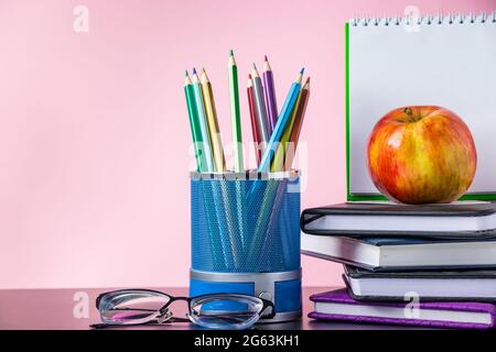 Zurück zum Schulkonzept. Schulbedarf, Bücher und Apfel auf rosa Hintergrund. Für Text platzieren. Stockfoto