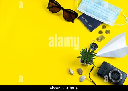 Reisepass, medizinische Maske und Sonnenbrille auf gelbem Hintergrund. Sicheres Reisekonzept während der Coronavirus-Pandemie. Flatlay, Kopierbereich. Stockfoto